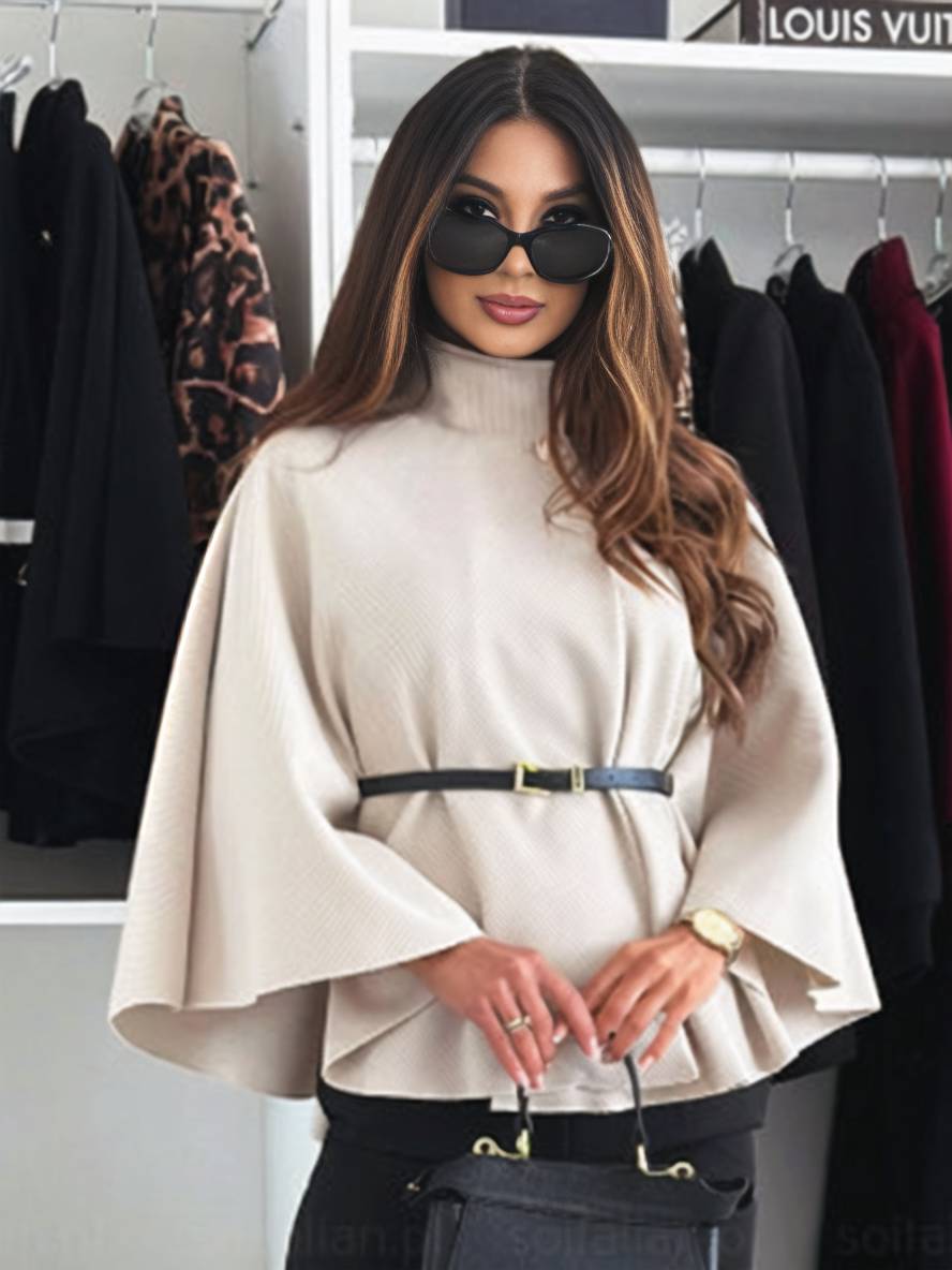 Frau mit Sonnenbrille und beigem Cape im Modegeschäft, umgeben von eleganter Kleidung. Stilvolle Mode, Damenbekleidung, Accessoires.