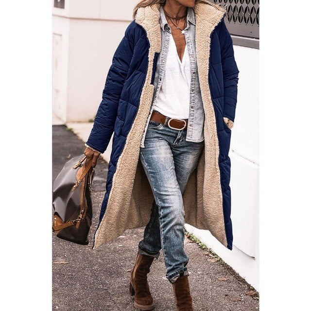 Frau in blauem, langem Wintermantel mit Fellfutter, Jeans und braunen Stiefeln, trägt braune Handtasche. Modischer Winterlook, Straßenstil.