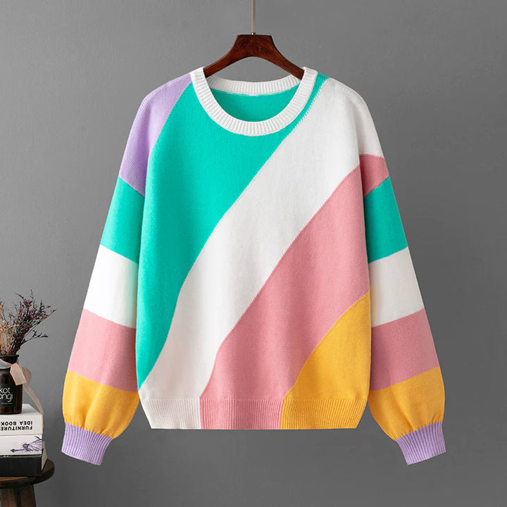 Bunter Pullover mit geometrischem Muster in Pastellfarben, hängend an einem Holzkleiderbügel vor grauem Hintergrund. Modetrend, Strickmode, Damenbekleidung.