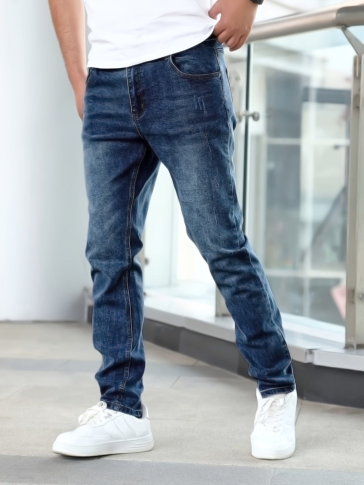 Mann in blauer Jeans und weißen Sneakern steht lässig an einem Geländer. Moderne Herrenmode, Freizeitlook, Denim-Jeans, urbane Kleidung.