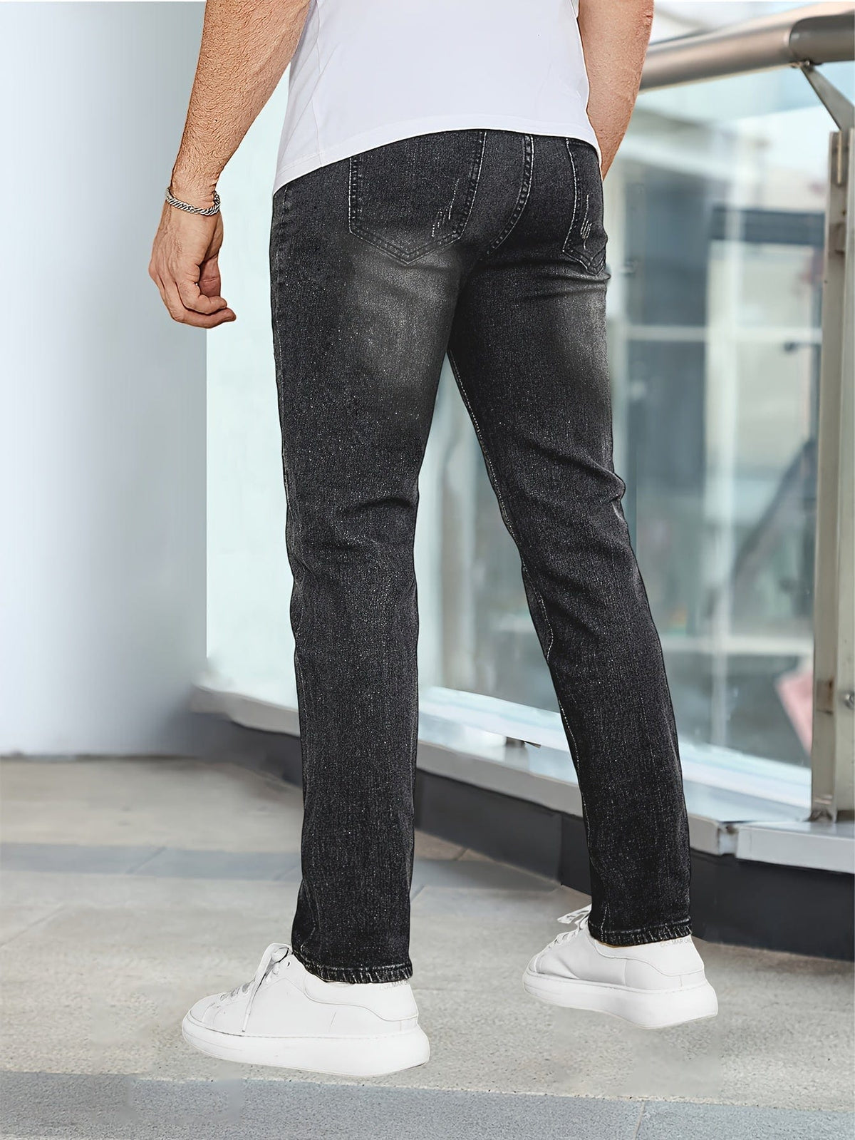 Mann in schwarzer Jeans und weißen Sneakern, Rückansicht. Moderne Herrenmode, lässiger Stil, urbaner Hintergrund.