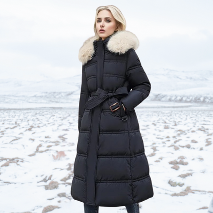 Frau in schwarzem Daunenmantel mit Fellkragen steht in verschneiter Landschaft. Wintermode, stilvoll, warm, Outdoor-Bekleidung.