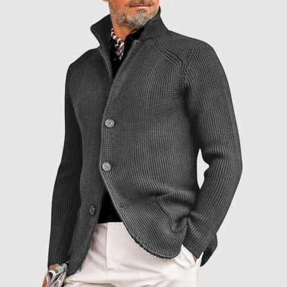 Grauer Herrenstrickjacke mit Stehkragen und Knopfleiste, kombiniert mit schwarzem Hemd und beiger Hose. Elegante Herrenmode, stilvoller Look.