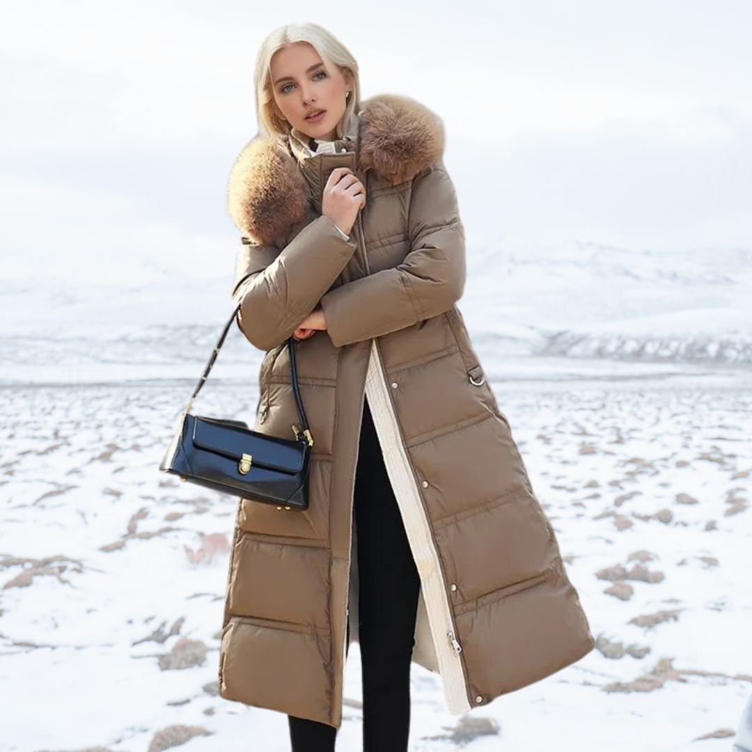 Frau in braunem Daunenmantel mit Pelzkragen, schwarze Handtasche, schneebedeckte Landschaft im Hintergrund. Wintermode, stilvoll, elegant.