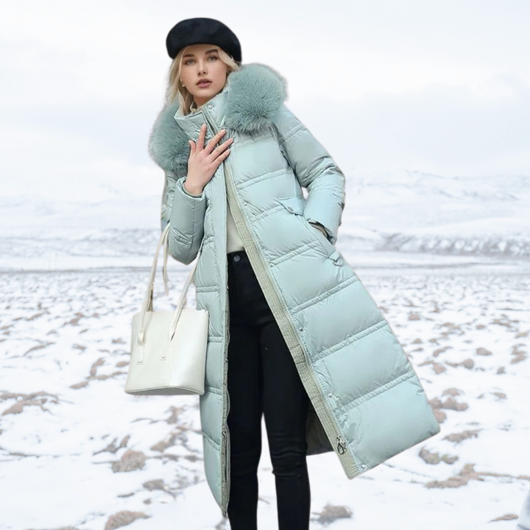 Frau in mintgrünem Daunenmantel mit Fellkapuze, schwarzer Mütze und weißer Tasche steht im verschneiten Winterlandschaft. Wintermode, Outdoor-Bekleidung.