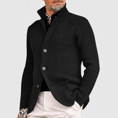 Mann in schwarzer Strickjacke mit Knöpfen, weißer Hose und Halstuch. Elegante Herrenmode, stilvoller Look, modische Herbstbekleidung.