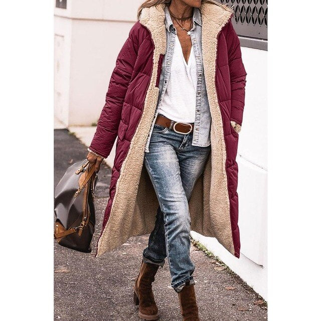 Frau in langem, weinrotem Wintermantel mit Fellfutter, Jeans und braunen Stiefeln, trägt braune Handtasche. Modischer Winterlook für Damen.