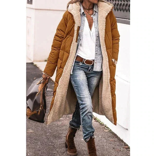 Frau in braunem Daunenmantel mit Fellfutter, Jeans und Stiefeln, trägt braune Tasche. Modischer Winterlook, lässig und stilvoll.