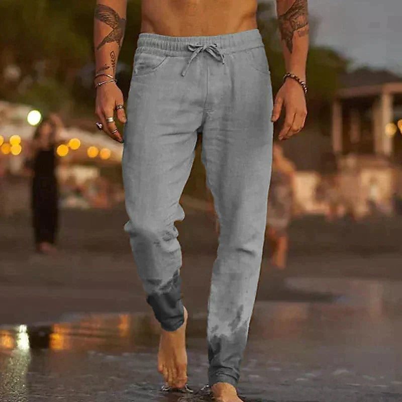 Mann in grauer Jogginghose geht barfuß am Strand entlang, Abendstimmung, Freizeitkleidung, Sommermode, entspannte Atmosphäre.