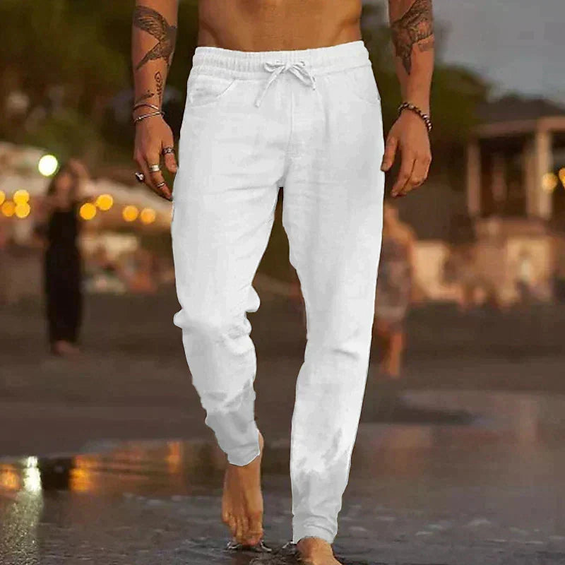 Ein Mann in weißen Leinenhosen spaziert barfuß am Strand entlang. Sommermode, Freizeitkleidung, Strandspaziergang, Herrenmode.
