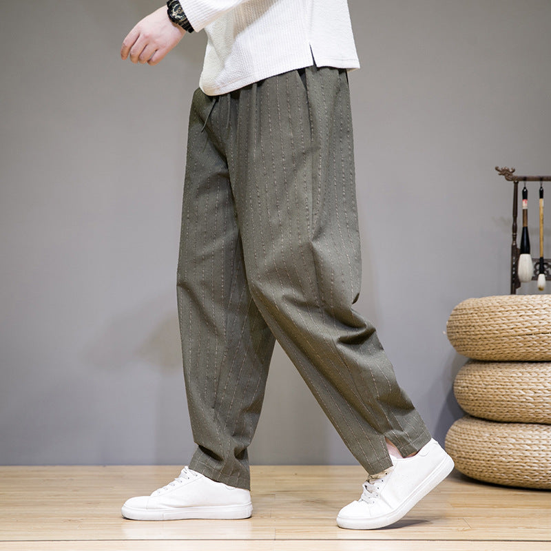 Person trägt weite, olivgrüne Hose mit Nadelstreifen und weiße Sneaker. Moderner, lässiger Stil, ideal für Freizeitmode und Streetwear.