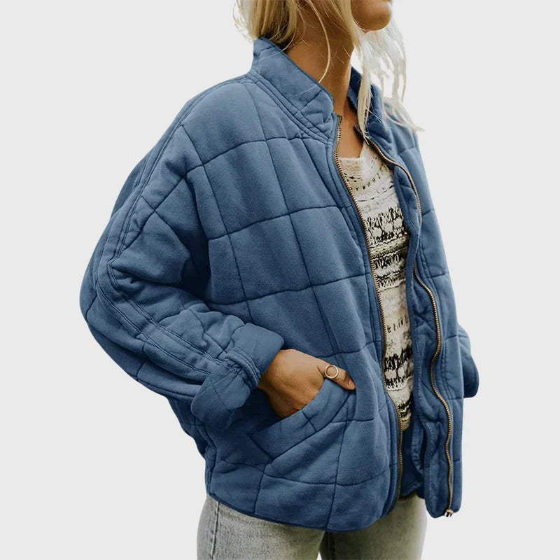 Frau in blauer Steppjacke, lässig offen getragen, mit weißem gemustertem Oberteil und Jeans. Modetrend, Damenbekleidung, Herbstmode.