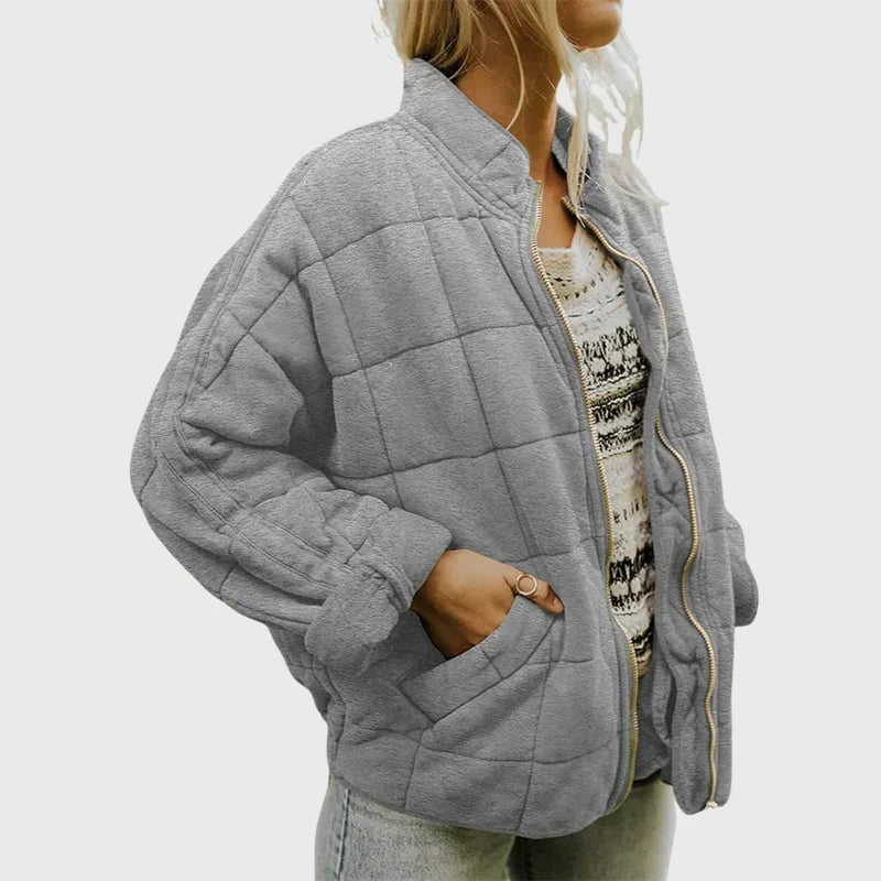 Frau in grauer Steppjacke mit Reißverschluss, lässig über gemustertem Pullover und Jeans getragen. Modetrend, Damenbekleidung, Herbstmode.