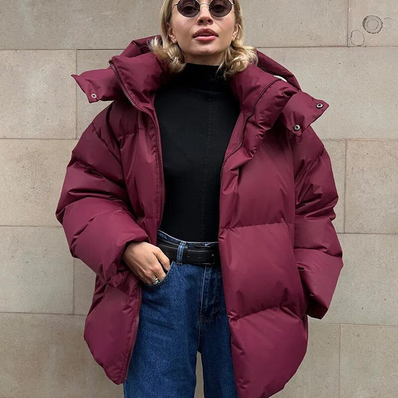 Frau in burgunderroter Daunenjacke, schwarzem Rollkragenpullover und blauer Jeans vor beiger Wand. Wintermode, stylische Damenbekleidung.