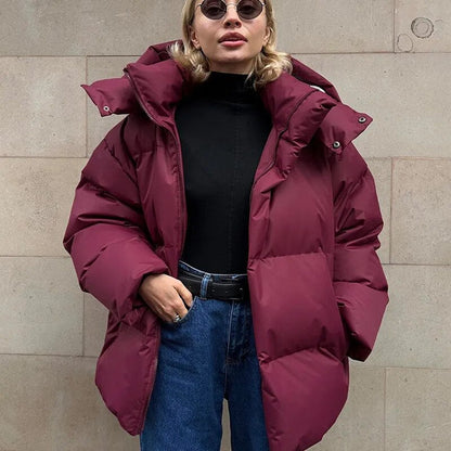 Frau in burgunderroter Daunenjacke, schwarzem Rollkragenpullover und blauer Jeans vor beiger Wand. Wintermode, stylische Damenbekleidung.