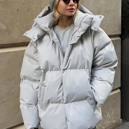Frau in grauer Daunenjacke und Mütze vor Betonwand. Wintermode, warme Kleidung, stilvolle Damenjacke, Outdoor-Bekleidung.