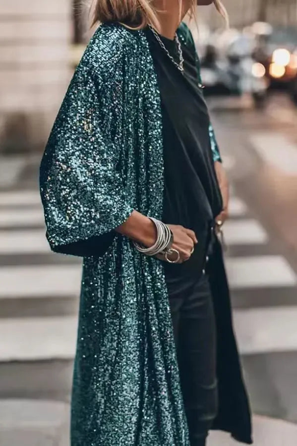 Frau in glitzerndem, türkisfarbenem Paillettenmantel, schwarzem T-Shirt und Jeans auf einer Stadtstraße. Modetrend, Streetstyle, elegantes Outfit.